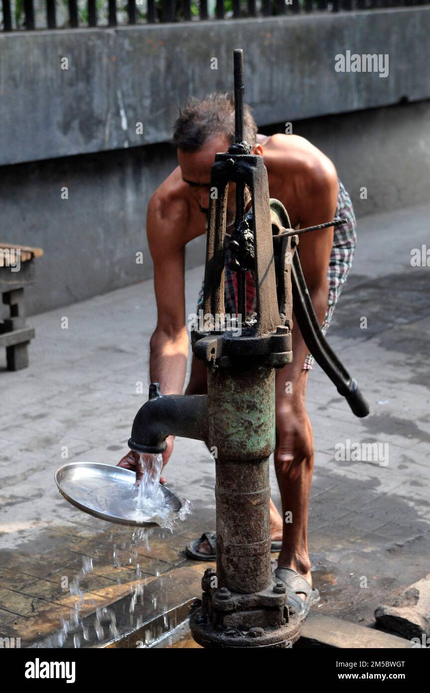 Un bengalese che lava il piatto da una pompa a mano nel centro di Kolkata, in India. Foto Stock