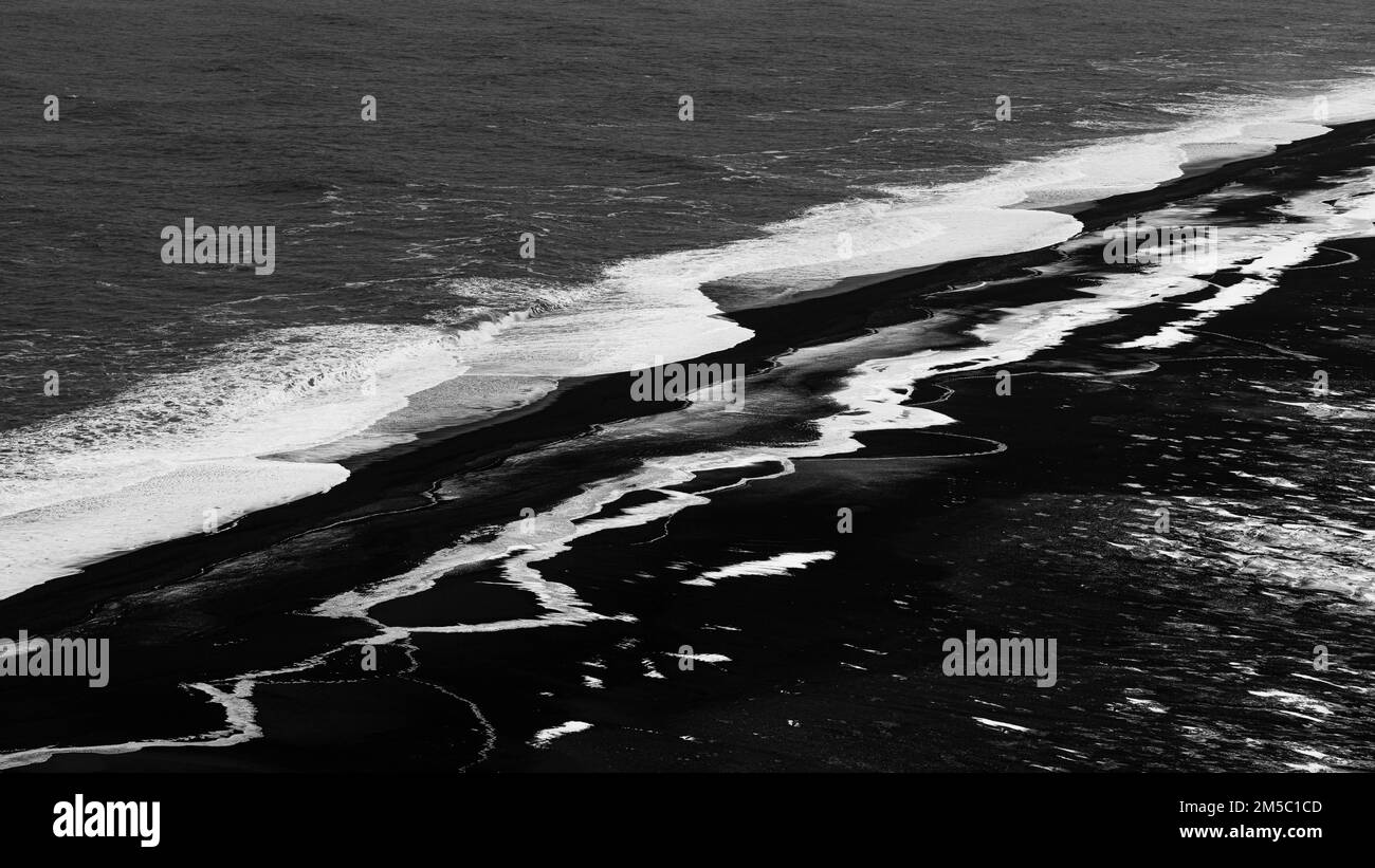 Onde bianche e superfici ghiacciate sulla spiaggia di ciottoli neri Skogarsandur, vicino a Dyrholaey, foto in bianco e nero, Sudurland, Islanda Foto Stock
