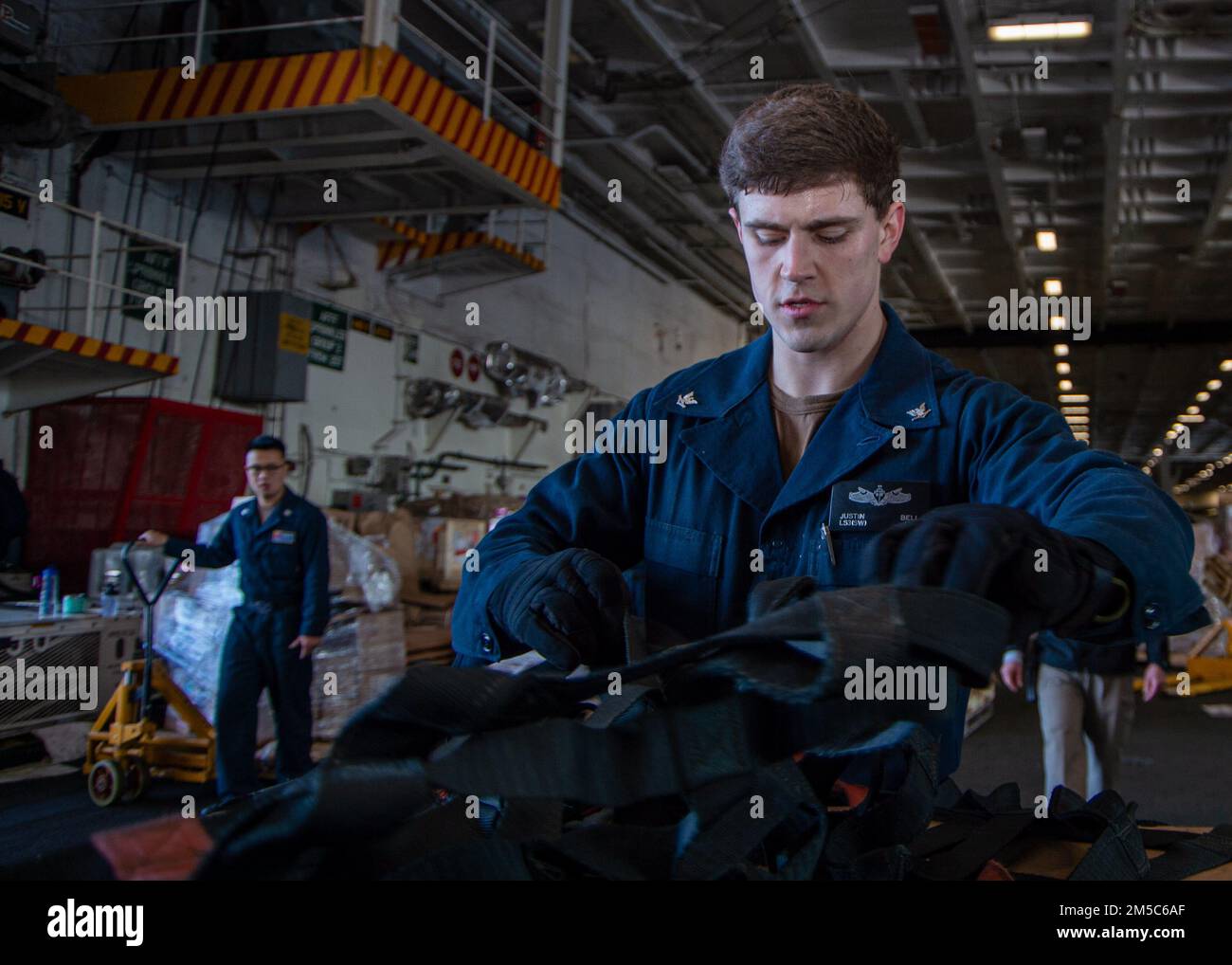 220228-N-JR318-1048 MARE ADRIATICO (28 febbraio 2022) Logistics Specialist 3rd Class Justin Bell, di Georgetown, Kentucky, rimuove le reti da carico nella baia hangar del portaerei di classe Nimitz USS Harry S. Truman (CVN 75) durante un rifornimento in mare, 28 febbraio 2022. Il gruppo Harry S. Truman Carrier Strike Group è in fase di implementazione pianificata negli Stati Uniti Sesta area di attività Fleet a sostegno degli interessi degli Stati Uniti, alleati e partner in Europa e Africa. Foto Stock