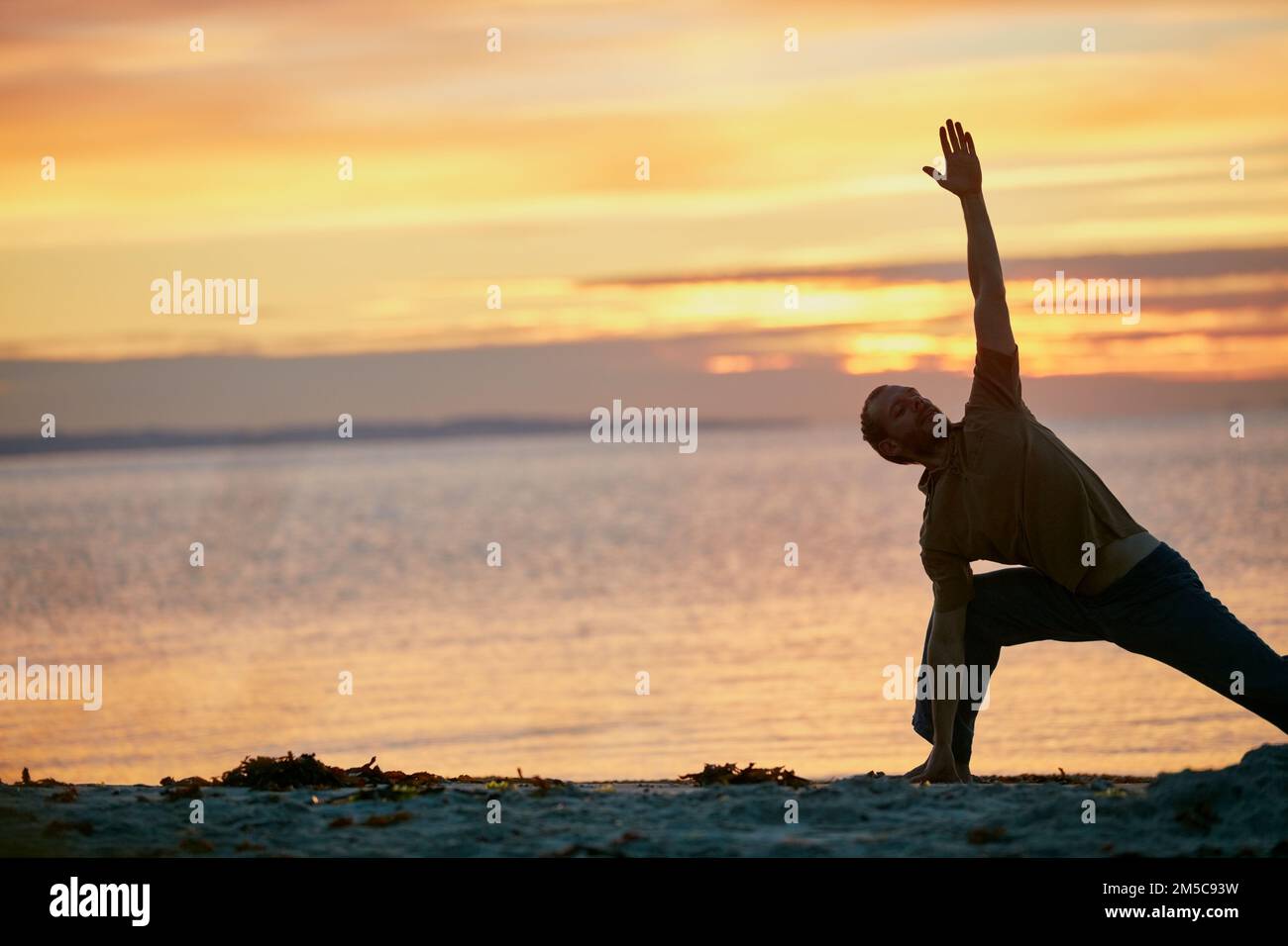 Allunga il corpo, allunga la mente. un uomo che pratica il triangolo posa durante la sua routine di yoga in spiaggia. Foto Stock