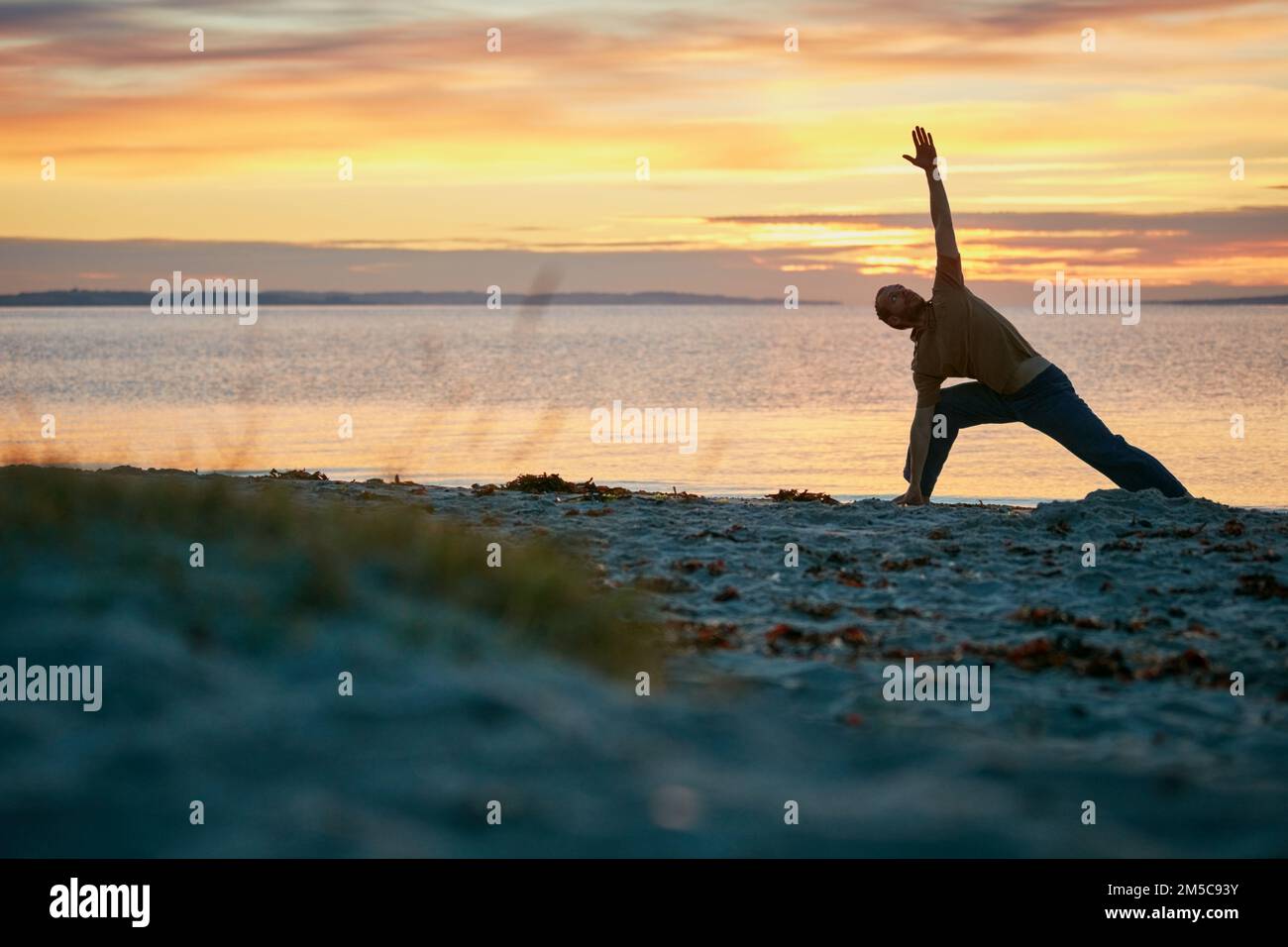 La pace è anche un super potere. un uomo che pratica il triangolo posa durante la sua routine di yoga in spiaggia. Foto Stock