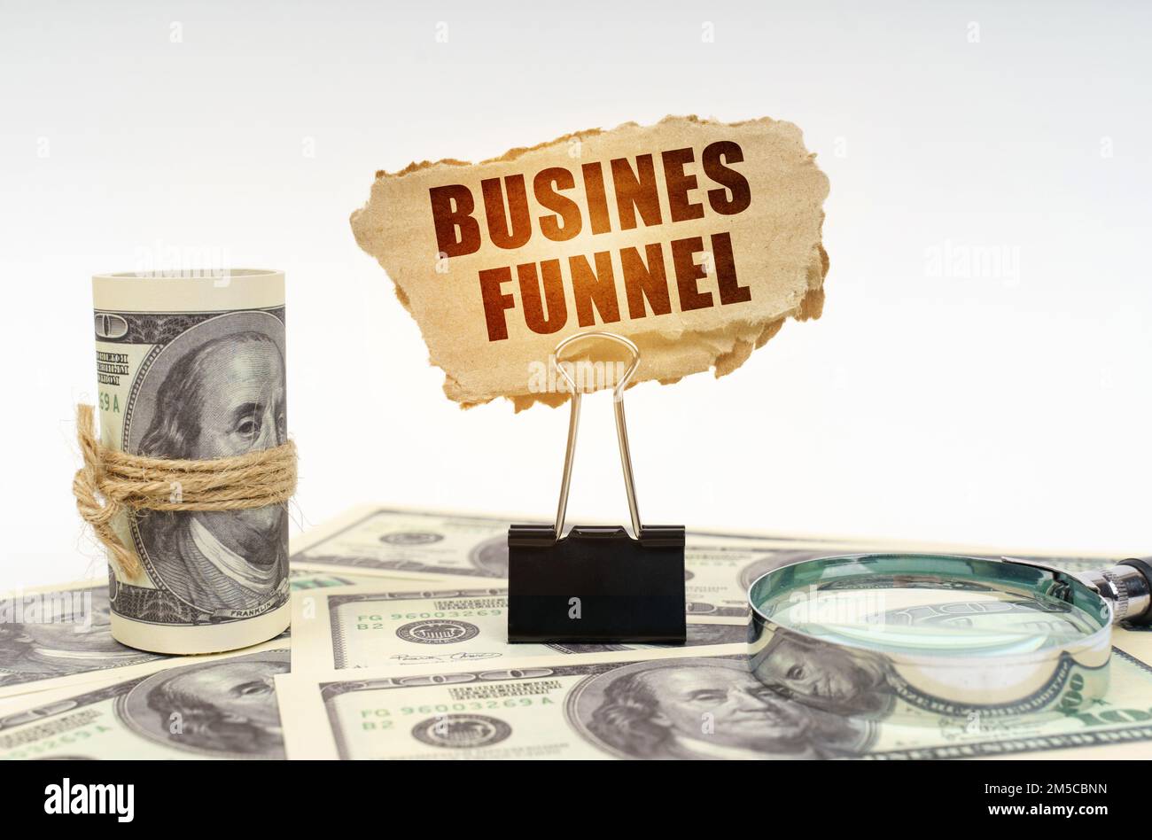 Concetto aziendale. Tra i dollari si trova una lente d'ingrandimento e vi è una clip e un segno di cartone con l'iscrizione - Business Funnel Foto Stock