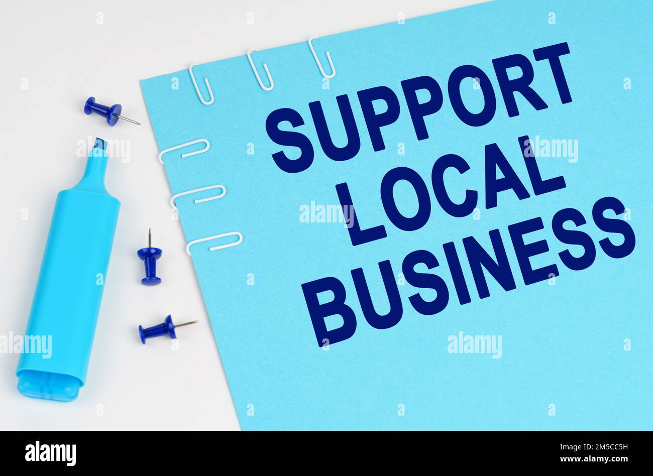 Concetto economico. Su una superficie bianca, un indicatore, pulsanti e un foglio di carta blu con l'iscrizione - supporto per l'azienda locale Foto Stock