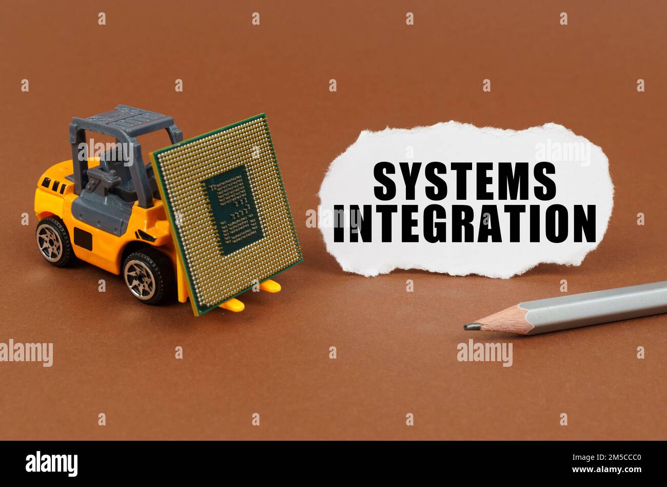 Concetto tecnologico. Su una superficie marrone, un carrello elevatore a forche trasporta un processore, accanto ad esso è presente un foglio con la scritta - Systems Integration Foto Stock