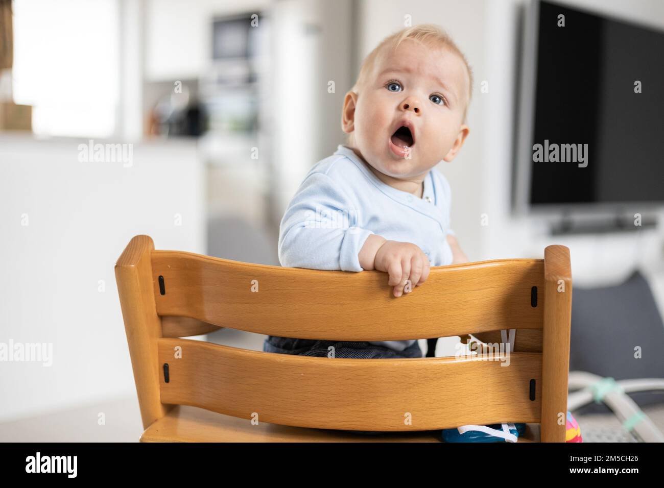 Felice bambino seduto in tradizionale design scandinavo seggiolone in legno in moderna casa luminosa. Bambino carino Foto Stock