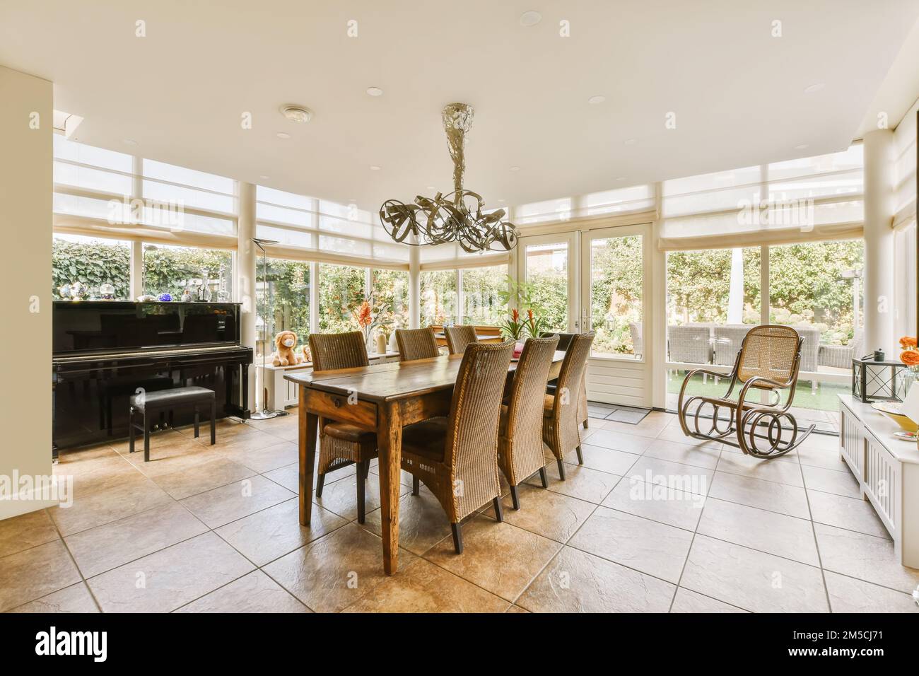 una sala da pranzo con un pianoforte al centro e una porta aperta che conduce all'area patio sull'altro lato Foto Stock