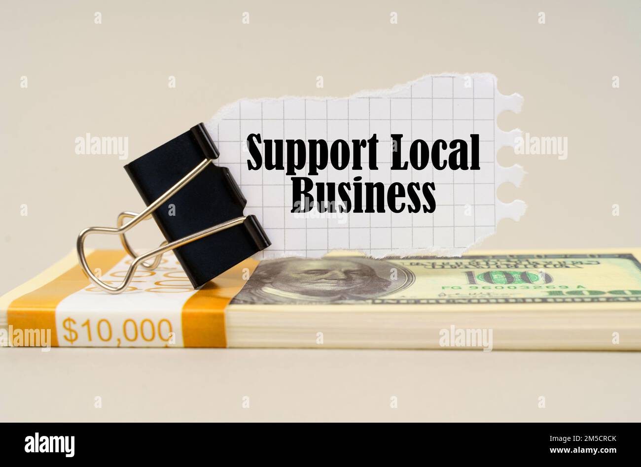 Concetto aziendale. Su una superficie grigia è una confezione di dollari su cui c'è una clip con carta strappata e l'iscrizione - Support Local Business Foto Stock