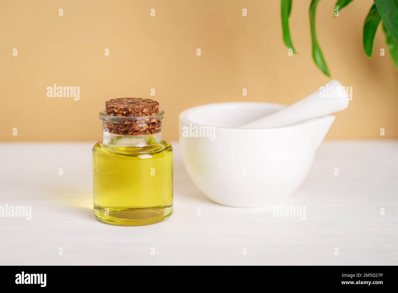 Olio base cosmetico naturale e Malta e pestello in ceramica bianca su tavola bianca su sfondo beige. Cosmetici naturali, prodotti per la cura della pelle e prodotti di bellezza Foto Stock