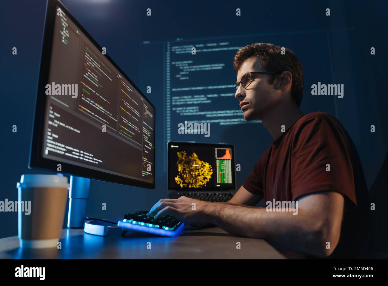 Immagine laterale di un moderno sviluppatore IT che utilizza il computer in ufficio di notte, lavora al software, codifica di una nuova applicazione, seduto di fronte al grande monitor del pc. Specialista in scienza dei dati al lavoro Foto Stock