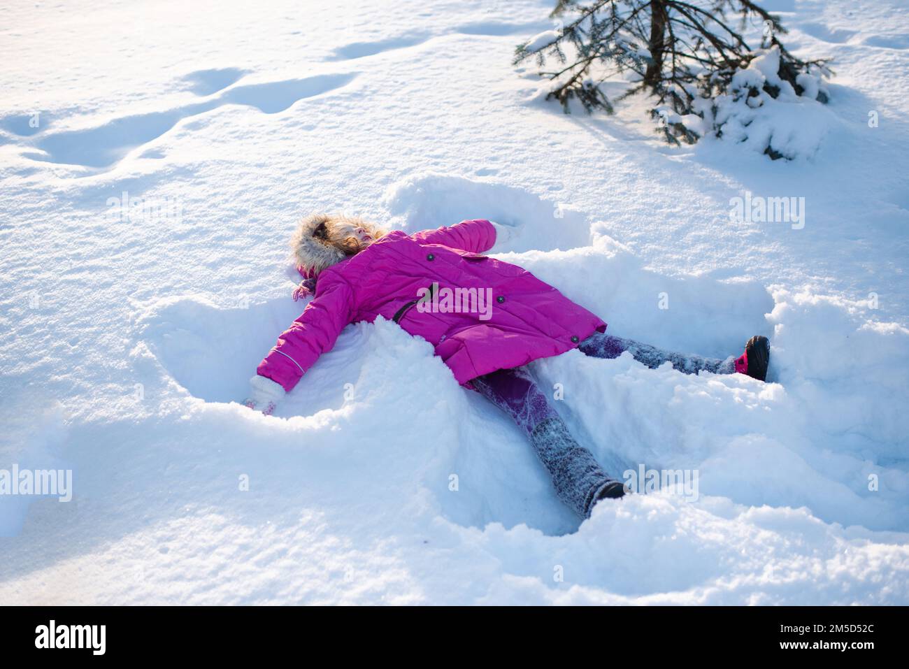 Ragazza cute sorridente bambino 5-6 anni sdraiato in neve che fa angelo forma all'aperto. Stagione invernale. Felicità. Foto Stock