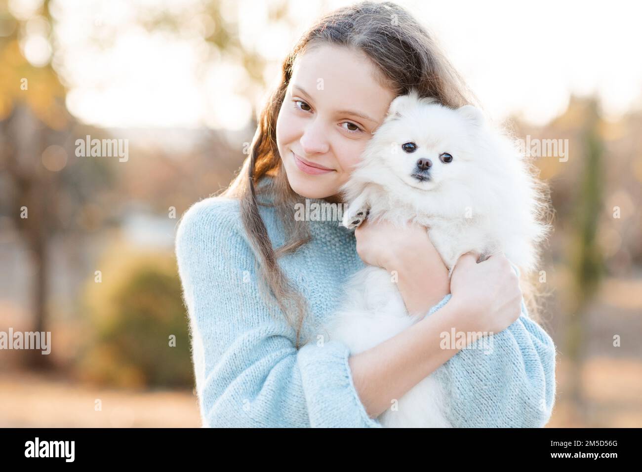 Ragazza giovane sorridente cute 15-16 anni tenendo bianco soffice cane cucciolo spitz insieme su sfondo giallo autunno natura nel parco. Amicizia. Foto Stock