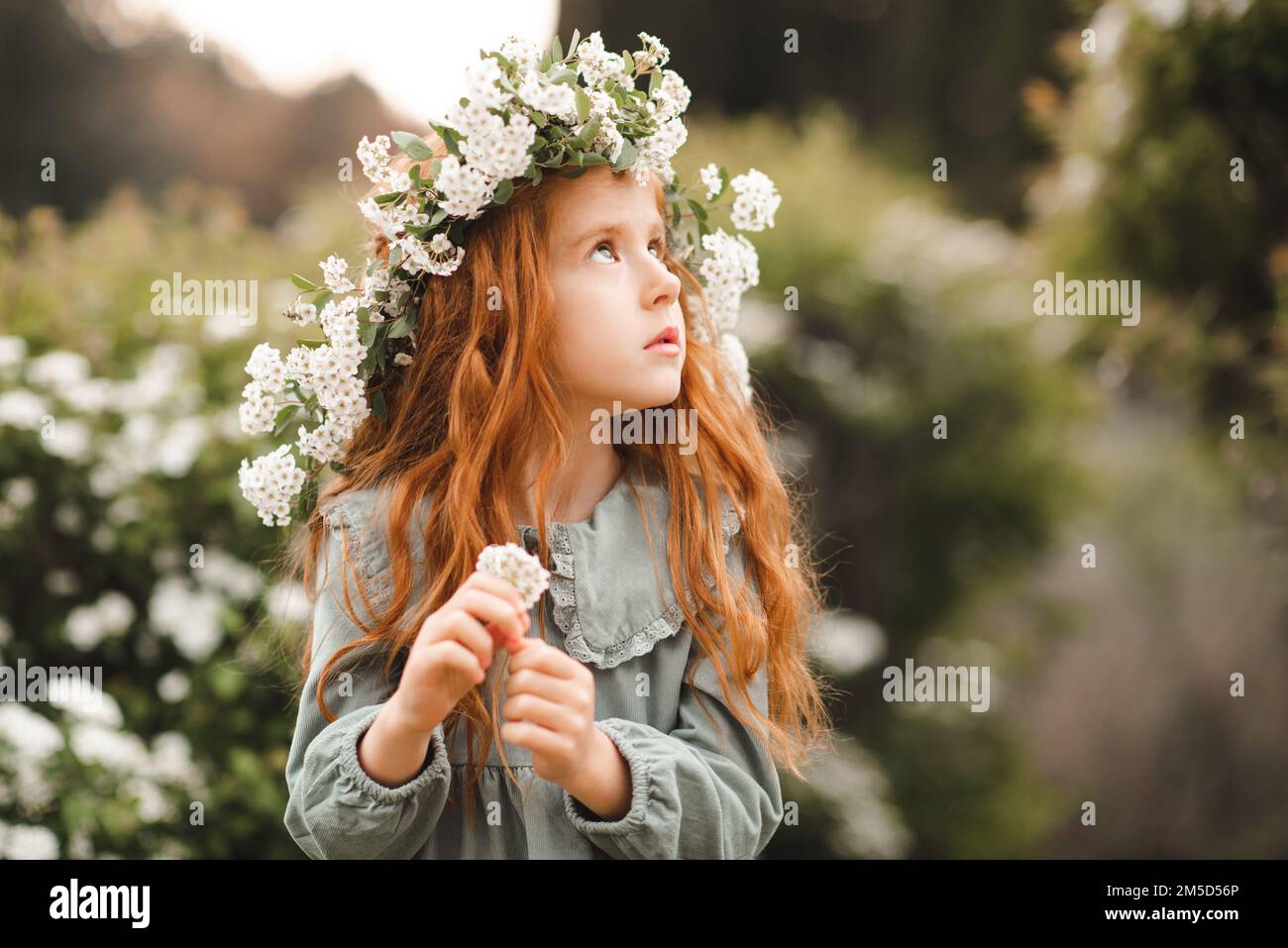 Ragazza cute bambino 4-5 anni indossare corona floreale e vintage vestito su sfondo floreale primo piano. Primavera. Foto Stock