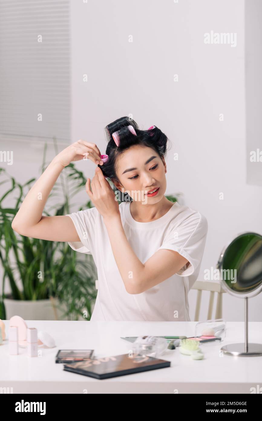 Bella giovane donna adulta in rullo per capelli guardando nello specchio Foto Stock