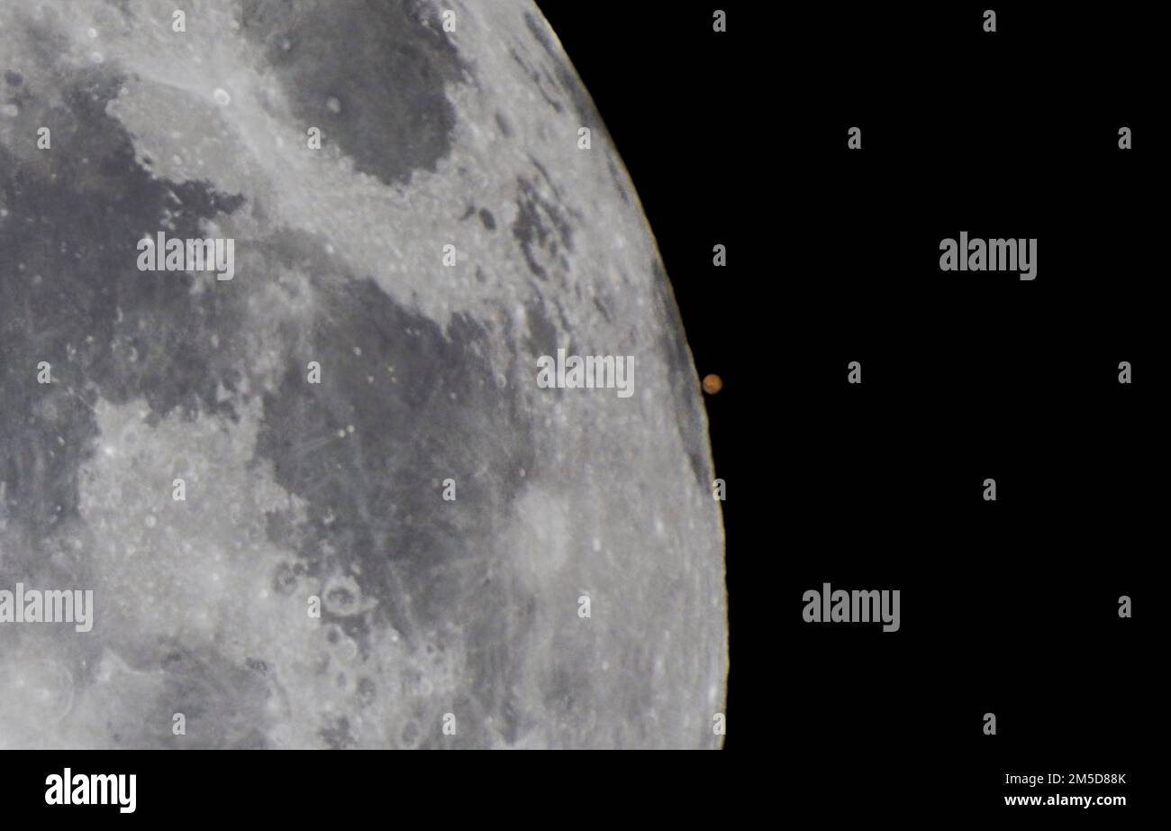 Una vista ravvicinata della riapparizione di Marte da dietro il disco della Luna piena, durante l'occultazione di Marte del 7 dicembre 2022. Alcune delle dar Foto Stock