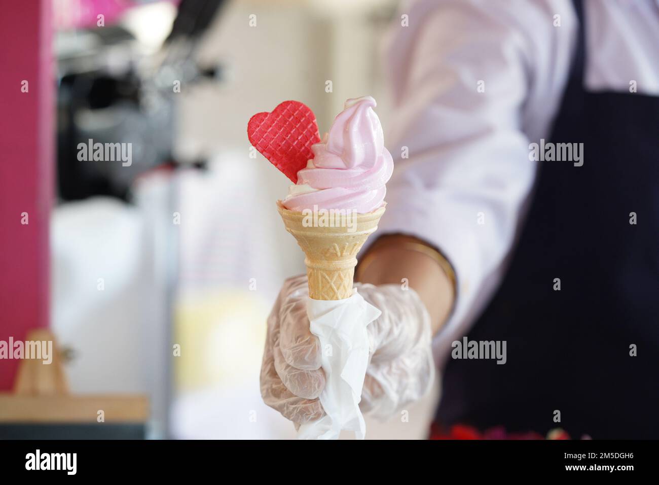 Un operaio con guanti in possesso di un cono gelato con un mix di sapori rosa e vaniglia. Gelato rosa con cuore rosso. Foto Stock