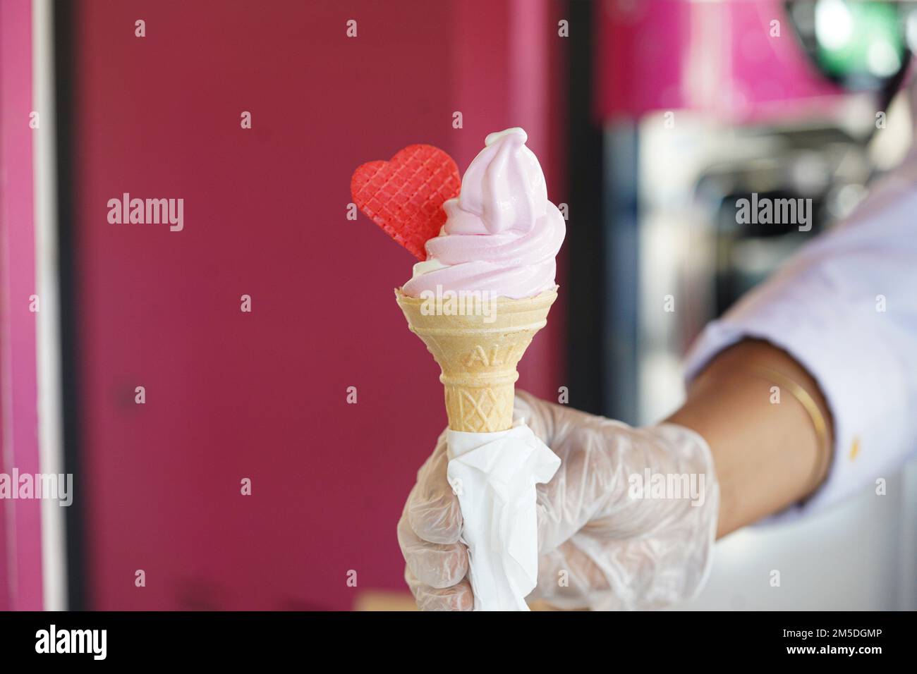 Un operaio con guanti in possesso di un cono gelato con un mix di sapori rosa e vaniglia. Gelato rosa con cuore rosso. Foto Stock