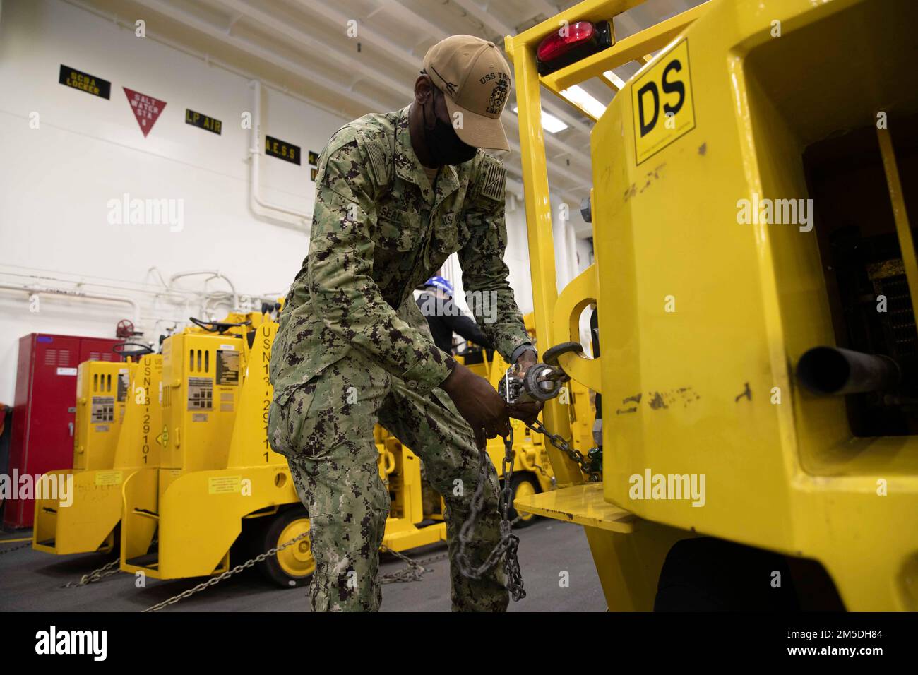 220304-N-VJ326-1064 SAN DIEGO (4 marzo 2022) – Aviation Electrician’s Mate 3rd Class Kyle Seal, di Detroit, regola una catena di ancoraggio nella baia di hangar a bordo di una nave d’assalto anfibia USS Tripoli (LHA 7), marzo 4. Tripoli è una nave d'assalto anfibio di classe americana ospita a San Diego. Foto Stock