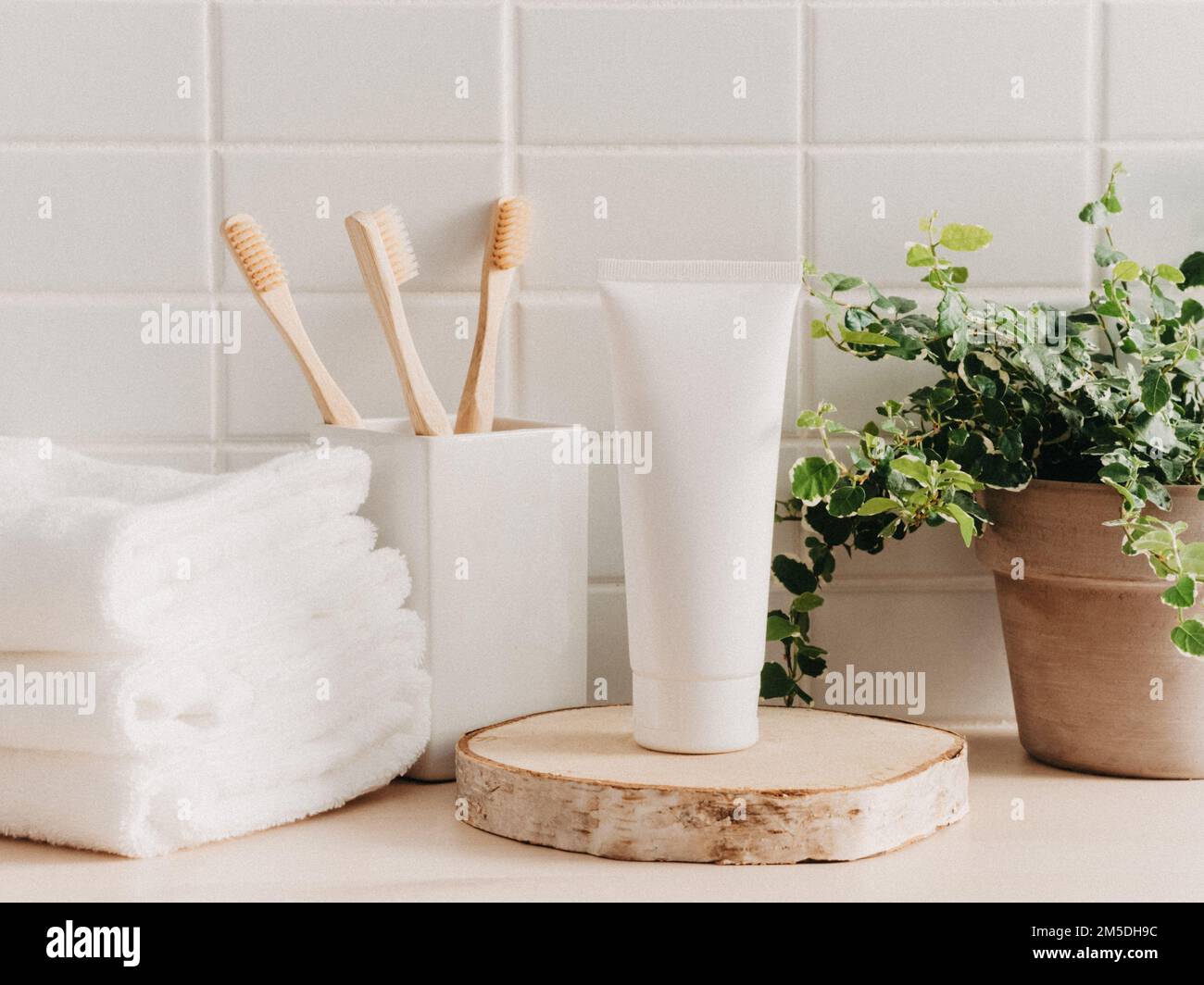 Tubo per prodotti cosmetici mockup su podio rotondo naturale e articoli da bagno su sfondo piastrellato bianco. Sfondo per la presentazione del cosmetico. Vista frontale Foto Stock