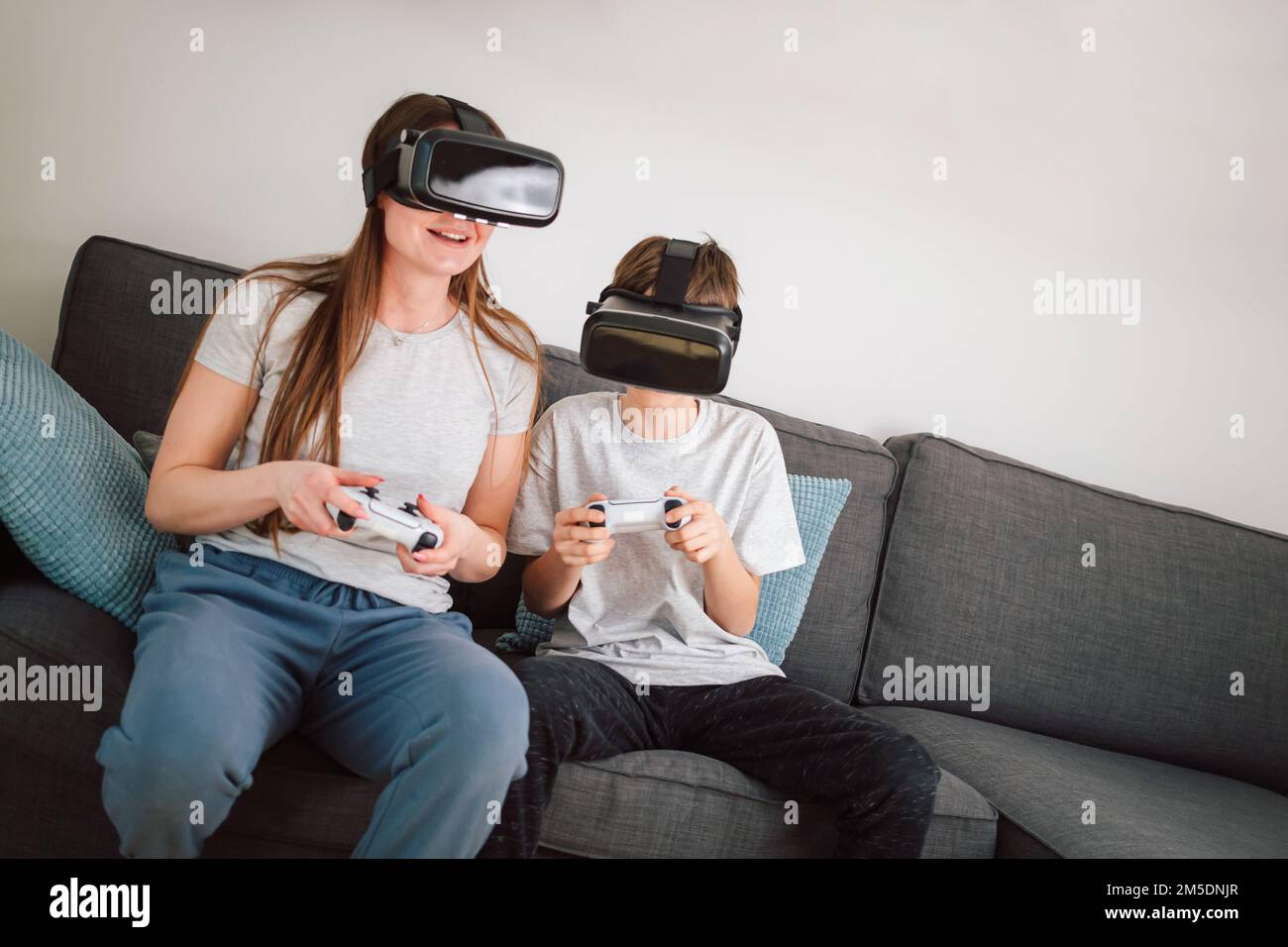 Madre e figlio amano giocare insieme con i videogame di intrattenimento, utilizzando gli occhiali e i controller VR seduti su un divano nel soggiorno Foto Stock