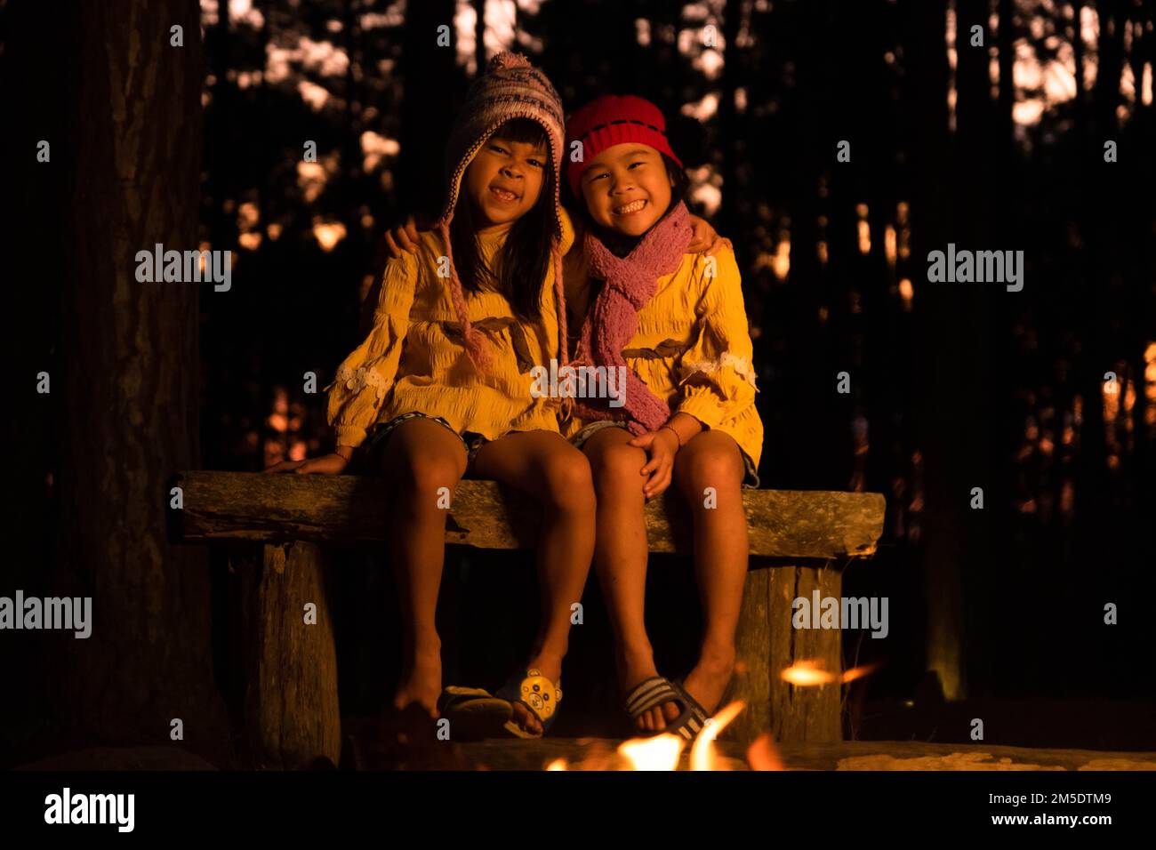 Carino piccole sorelle caldo vicino al fuoco all'aperto in tempo freddo. Bambini che si divertono al fuoco del campo. Campeggio con bambini in pineta invernale. Felice Foto Stock