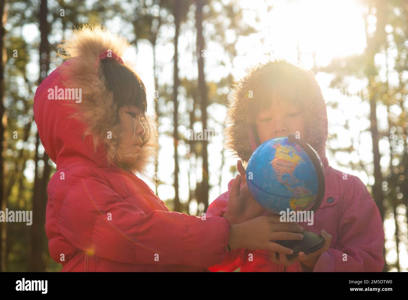 Due ragazze asiatiche carine imparando un modello del mondo sullo sfondo della natura e la luce calda del sole nel parco. I bambini imparano attraverso attività educative di gioco Foto Stock