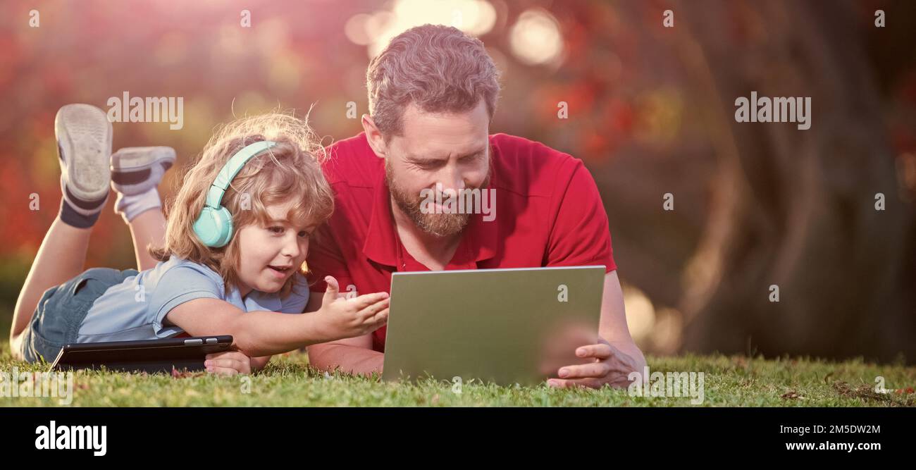 Banner di padre su figlio ragazzo scuola con notebook studio online giacendo su erba, blog di famiglia. Infanzia e paternità. Ragazzo felice ascoltare musica in Foto Stock