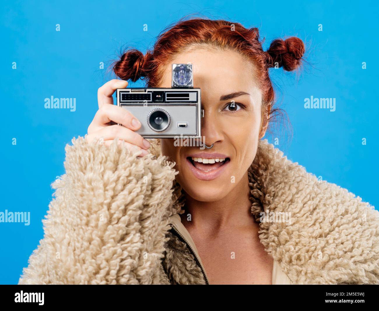 Bella testa rossa con una fotocamera vintage 35mm con flash cubo su sfondo blu. Foto Stock