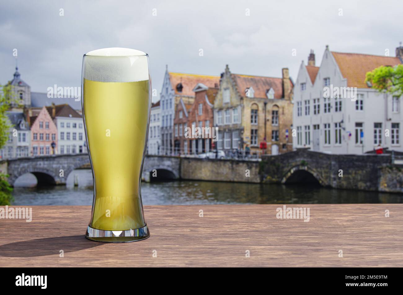 Bicchiere di birra leggera su un tavolo di legno con vista sul canale e sulla strada di Bruges, Belgio Foto Stock