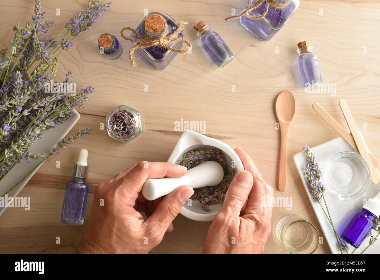 Persona che fa l'essenza fatta in casa di lavanda con punte naturali di lavanda, vasi e attrezzi per la preparazione su tavola di legno. Vista dall'alto. Foto Stock