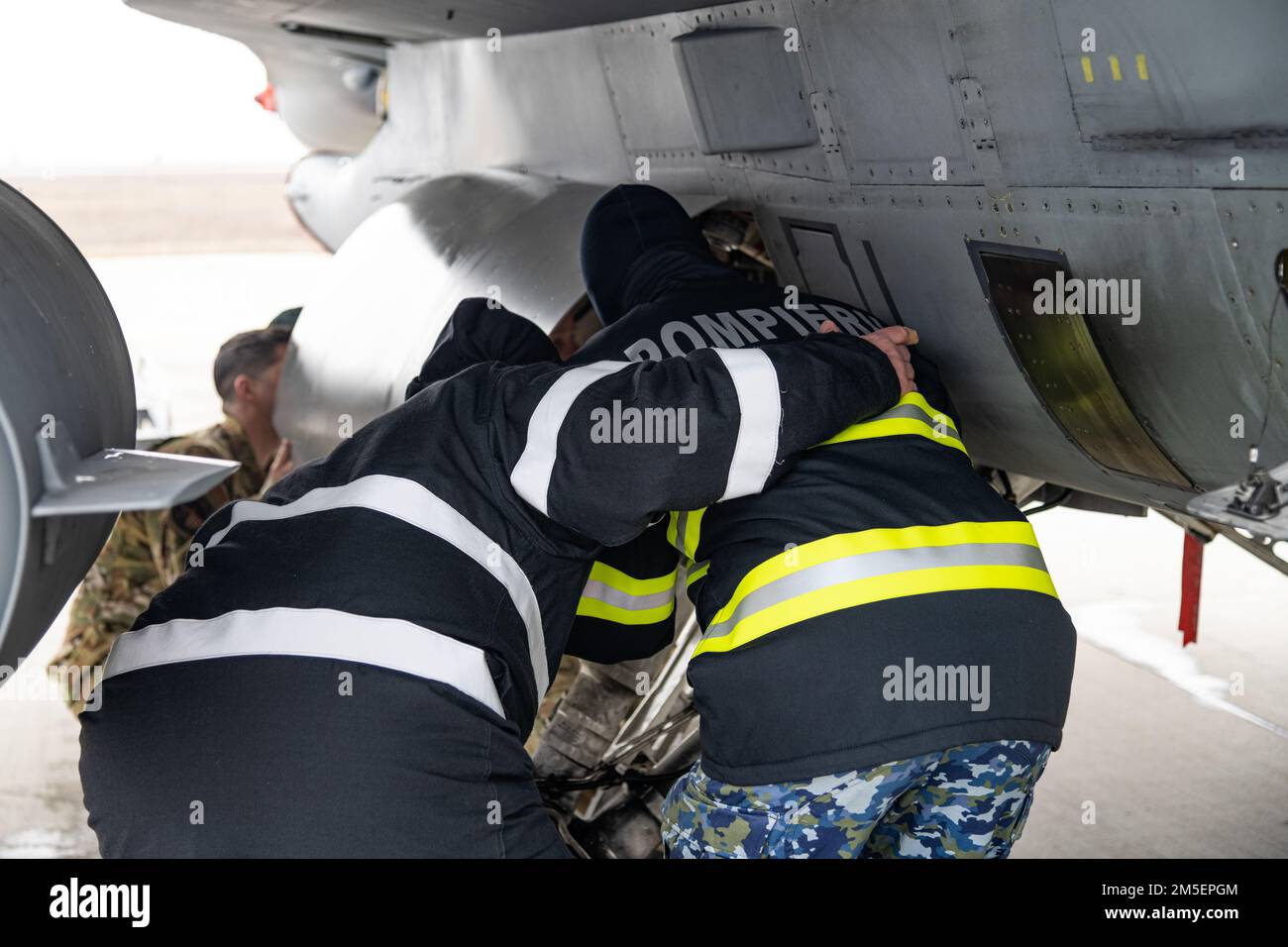 Due vigili del fuoco dell'aeronautica rumena della base aerea 86th, Romania, osservano gli Stati Uniti I vigili del fuoco dell'aeronautica dimostrano come gestire correttamente le emergenze e salvare i piloti da un aereo Falcon combattente F-16. Il rafforzamento delle relazioni con gli alleati della NATO garantisce che le forze aeree alleate possano collaborare per promuovere la pace nel teatro europeo, promuovendo al contempo il sostegno e l'interoperabilità. Foto Stock