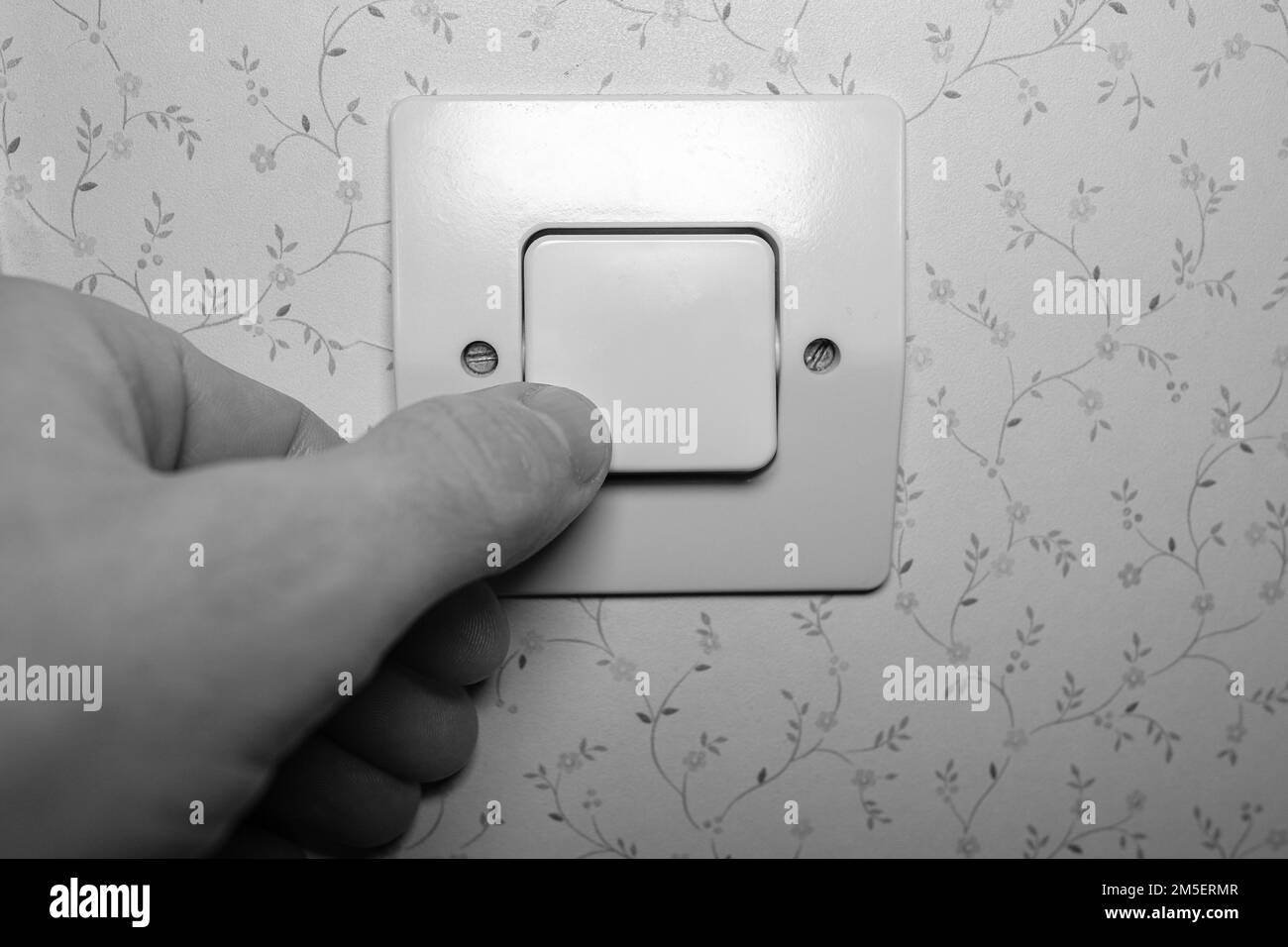 Aumento dei costi dell'elettricità in crisi, l'uomo accende le luci a casa, primo piano a mano in bianco e nero Foto Stock