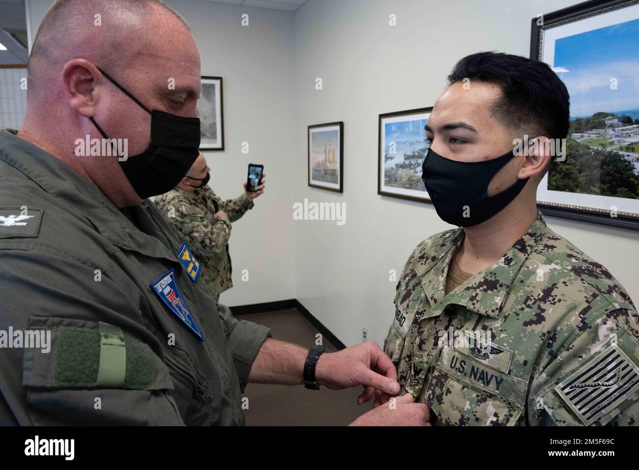 Patrick Dziekan, comandante, Fleet Activities Okinawa (CFAO) comandante ufficiale, promuove meritoriosamente Logistics Specialist 1st Class Bienvenido Quimbao, da Olongapo City, Filippine e assegnato alle operazioni portuali della CFAO, in una cerimonia sulla White Beach Naval Facility 10 10 marzo 2022 2022. La sua famiglia ha guardato la cerimonia tramite telefono cellulare. Il Meritorious Advancement Program consente agli ufficiali di comando di promuovere il personale idoneo al livello salariale successivo più elevato. Il programma è inteso a dare agli ufficiali di comando l'opportunità di riconoscere i loro migliori marinai da un Foto Stock