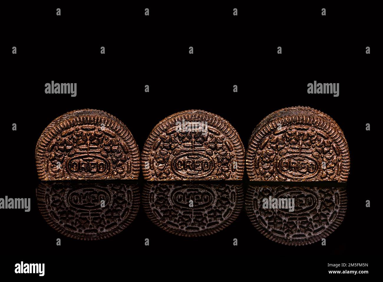 Tre biscotti Oreo riflessi sulla superficie nera su sfondo nero Foto Stock