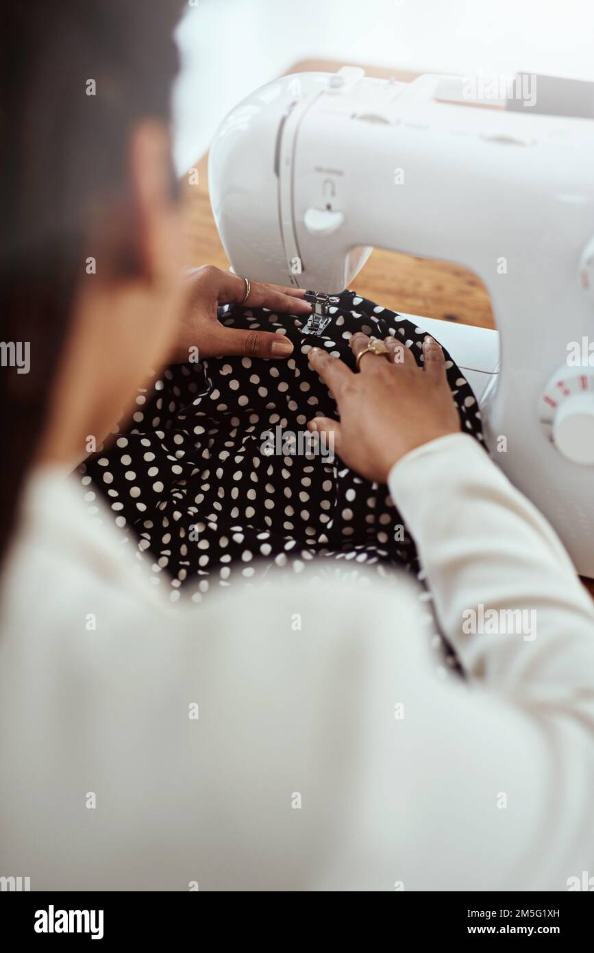 Il tocco finale. Ripresa da dietro di un giovane stilista di moda utilizzando una macchina da cucire nella sua officina. Foto Stock
