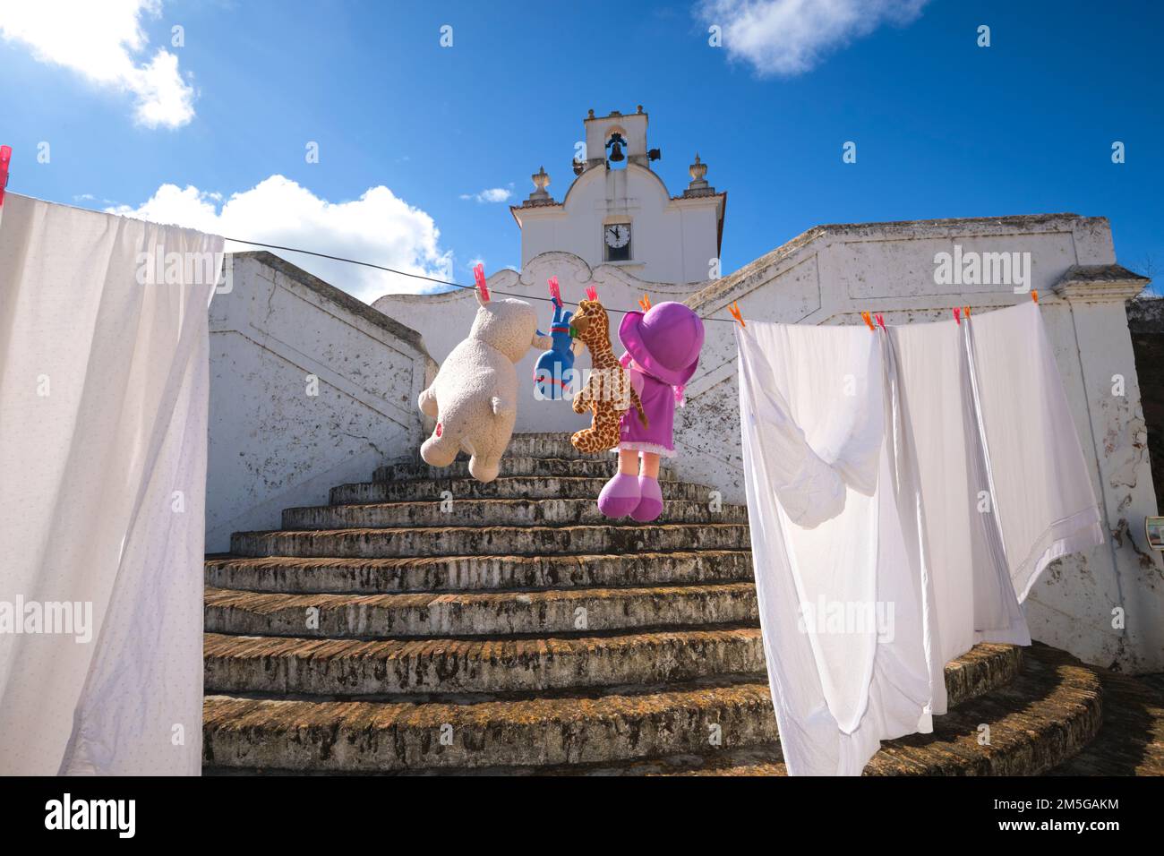 Una linea di lavanderia con divertenti animali farciti, bambole, appesi vicino alla vecchia chiesa moresca imbiancata. Nel comune di Alcoutim, nell'Algarve del po Foto Stock