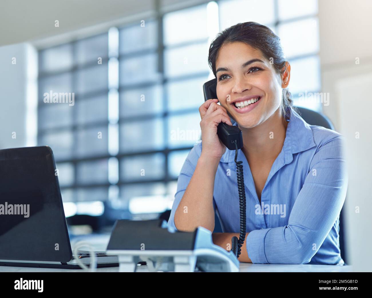 Con chi posso connetterti. una giovane donna d'affari che risponde a un telefono mentre usa il suo laptop alla sua scrivania. Foto Stock