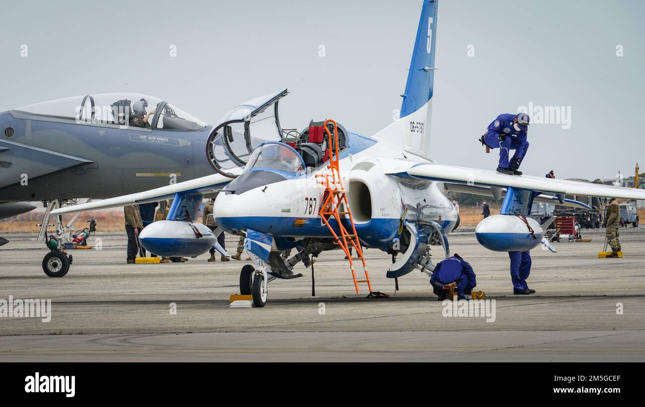 NEGLI STATI UNITI Air Force F-15C Eagle assegnata al 44th Fighter Squadron, Kadena Air base, Giappone, taxi per il suo parcheggio presso la Japan Air Self-Defense Force Tsuiki Air base, mentre i membri del Blue Impulse di JASDF eseguono controlli pre-volo, il 17 marzo 2022. La base aerea di Tsuiki sta ospitando l'iterazione corrente del programma di trasferimento di addestramento di aeronautica che aumenta la preparazione operativa e migliora l'interoperabilità con i nostri alleati giapponesi. Foto Stock