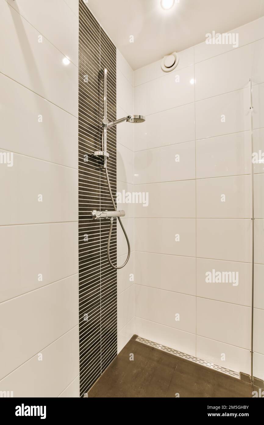 un bagno moderno con piastrelle bianche e nere alle pareti, poggiatesta per  doccia e poggiapiedi a mano contro la parete Foto stock - Alamy