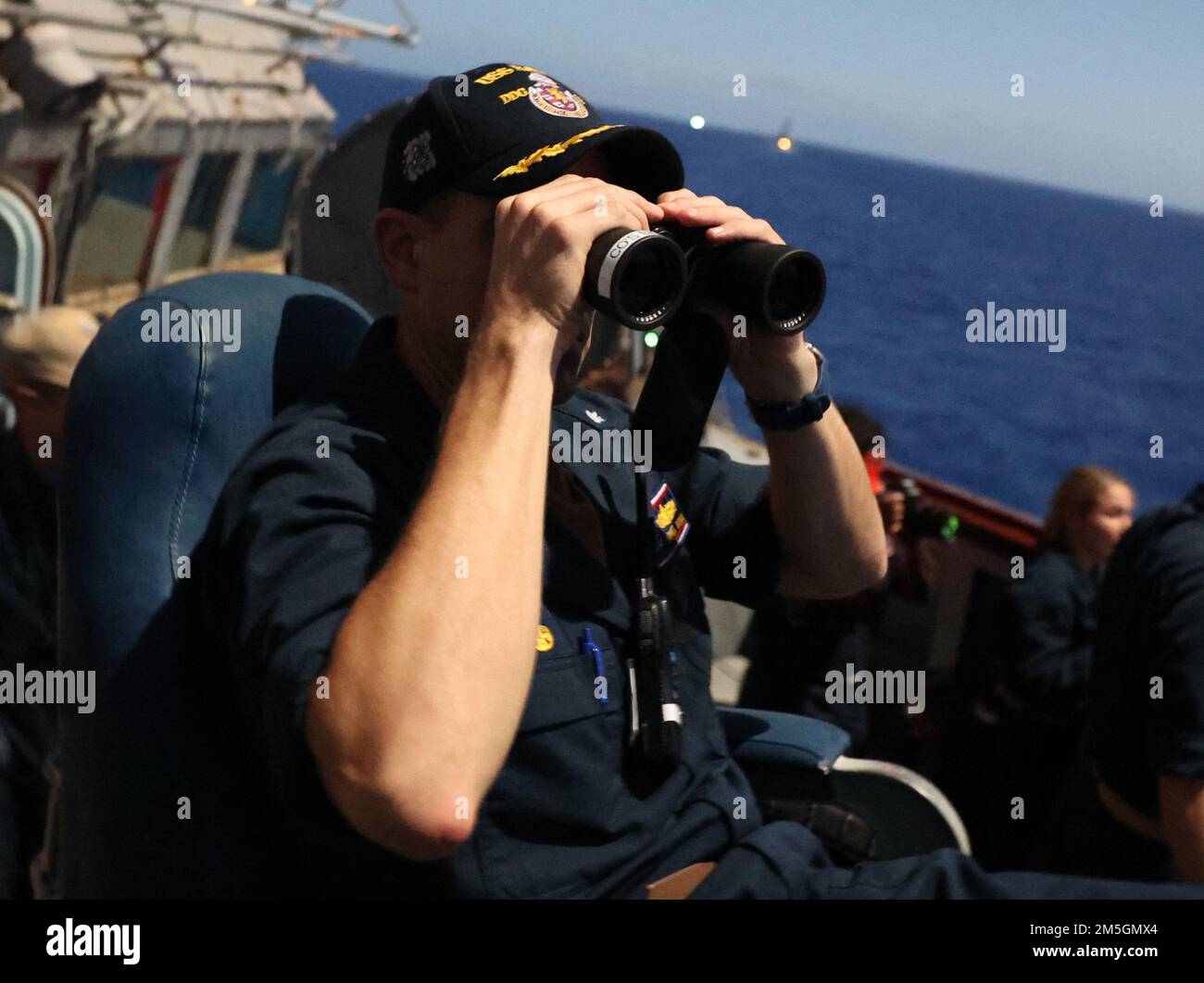 220317-N-CX281-1003 MARE DELLE FILIPPINE (17 marzo 2022) CMdR. Grant Bryan, comandante ufficiale del cacciatorpediniere missilistico guidato della classe Arleigh-Burke USS Barry (DDG 52), scandisce l'orizzonte durante un esercizio di allenamento notturno. USS Barry è assegnato a Destroyer Squadron (DESRON) 15 ed è in corso il supporto di un libero e aperto Indo-Pacific. CTF 71/DESRON 15 è la più grande DESRON della Marina e la principale forza di superficie della flotta statunitense 7th. Foto Stock