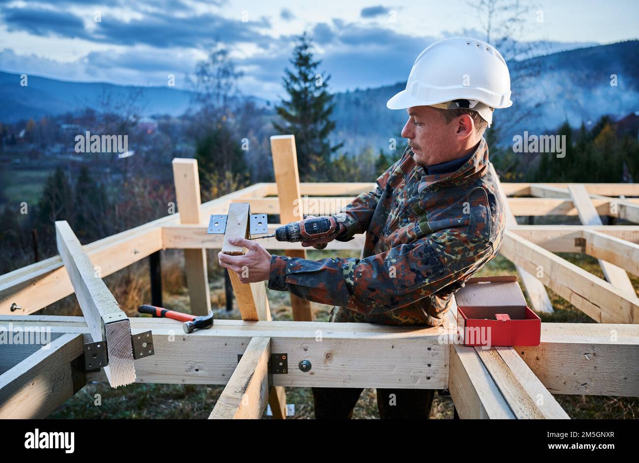 Uomo lavoratore costruire casa di legno telaio su palo fondazione. Carpentiere per l'installazione di mobili per travi in legno, con martello e cacciavite. Concetto di carpenteria. Foto Stock