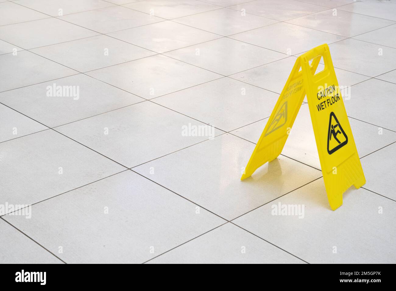 Cartello di pericolo di slittamento giallo pavimento bagnato su un pavimento piastrellato Foto Stock