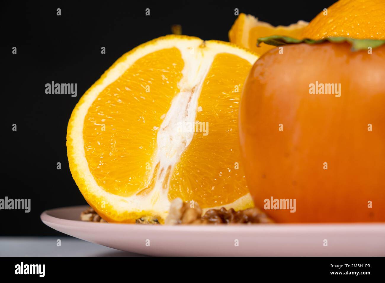 Mezzo arancione e un persimmon su un piatto su sfondo nero, spazio copia Foto Stock