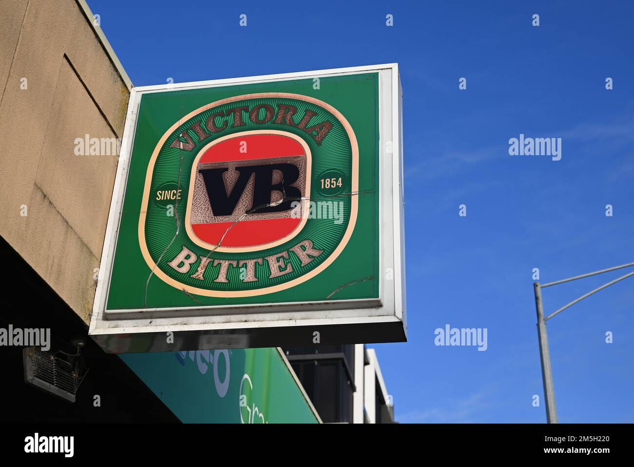 Victoria Bitter verde incrinato e stagionato, o VB, segno sopra un negozio, con il cielo blu sullo sfondo Foto Stock