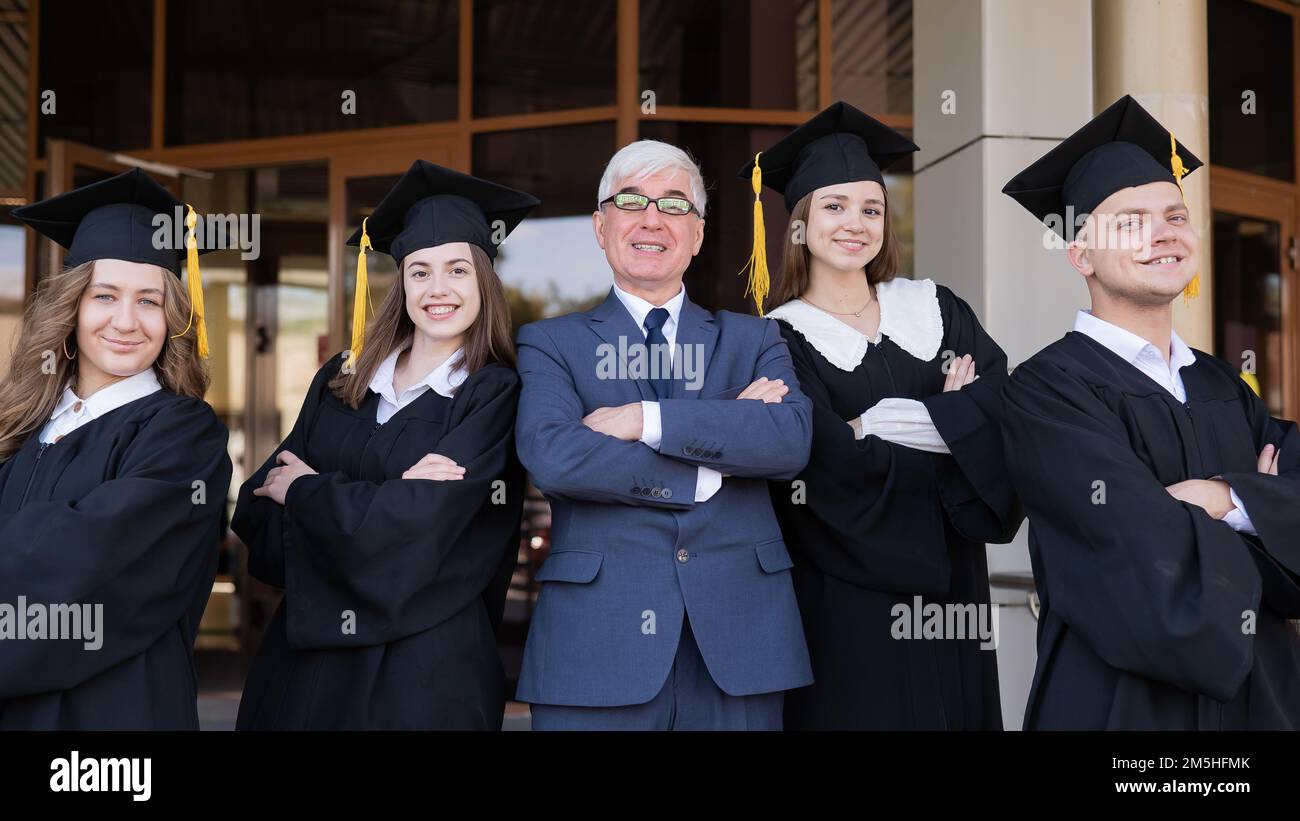 Un professore e i suoi studenti in abiti di laurea con le braccia incrociate sulle loro casse. Foto Stock