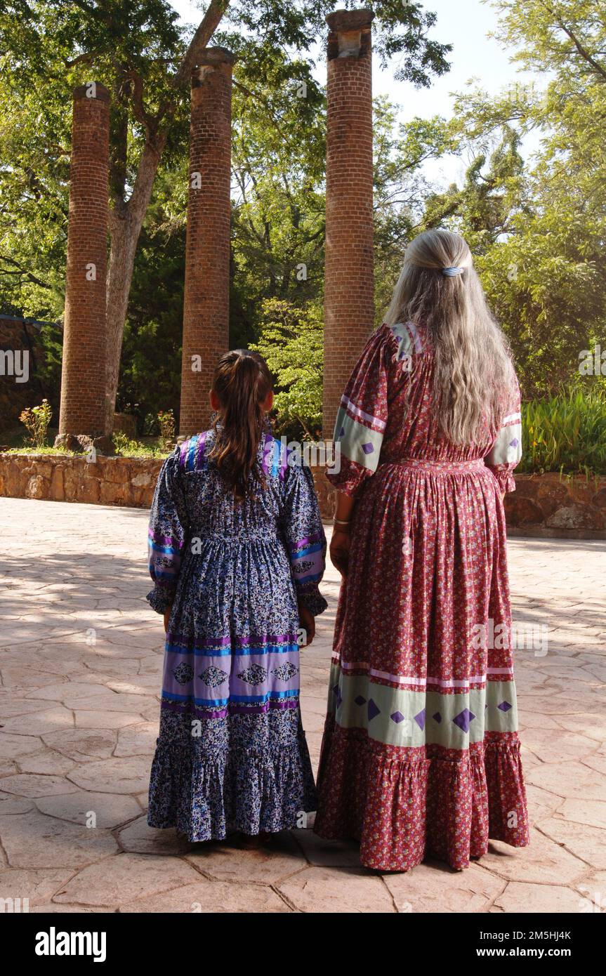 Cherokee Hills Byway - matriarca Cherokee e bambino presso le colonne del Seminario femminile Cherokee originale. Un matriarca Cherokee si erge con un bambino all'ombra di alberi e colonne. Il Cherokee Female Seminary è stato il primo e più raffinato istituto di istruzione superiore per le donne ad ovest del fiume Mississippi. Immaginate che il vecchio Cherokee insegnasse al bambino l'importanza dell'istruzione per il popolo Cherokee oggi, proprio come nel 1851. Location: Italy Foto Stock