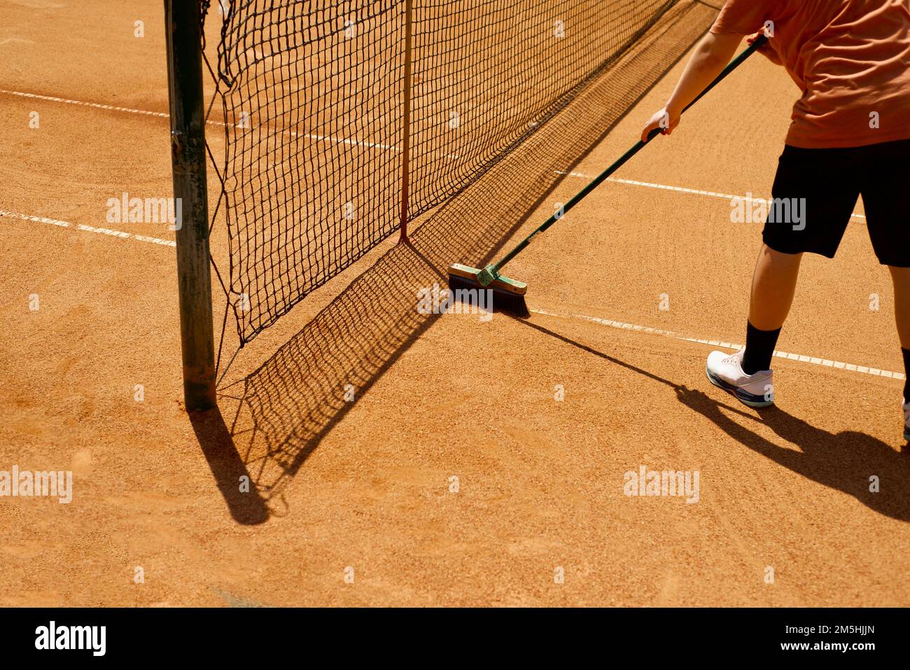 Manutenzione del campo da tennis. Linee di spazzolatura su un campo da tennis in argilla. Griglia e ombra. Gambe e mani di un adolescente. Foto Stock