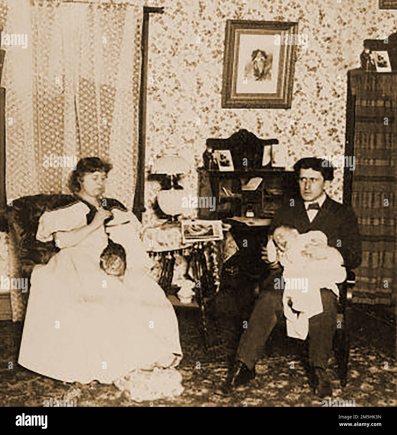 1897 - Una scena domestica in una famiglia vittoriana di classe media. Il padre nutre il bambino mentre la madre fa il suo lavoro artigianale, seminando o coccolando. Foto Stock