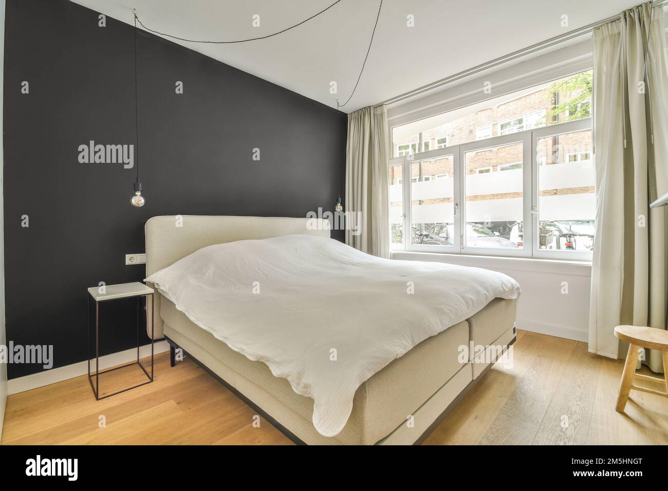 una camera da letto con pareti nere e letti bianchi, pavimento in legno e grandi finestre nella camera e' luminosa Foto Stock