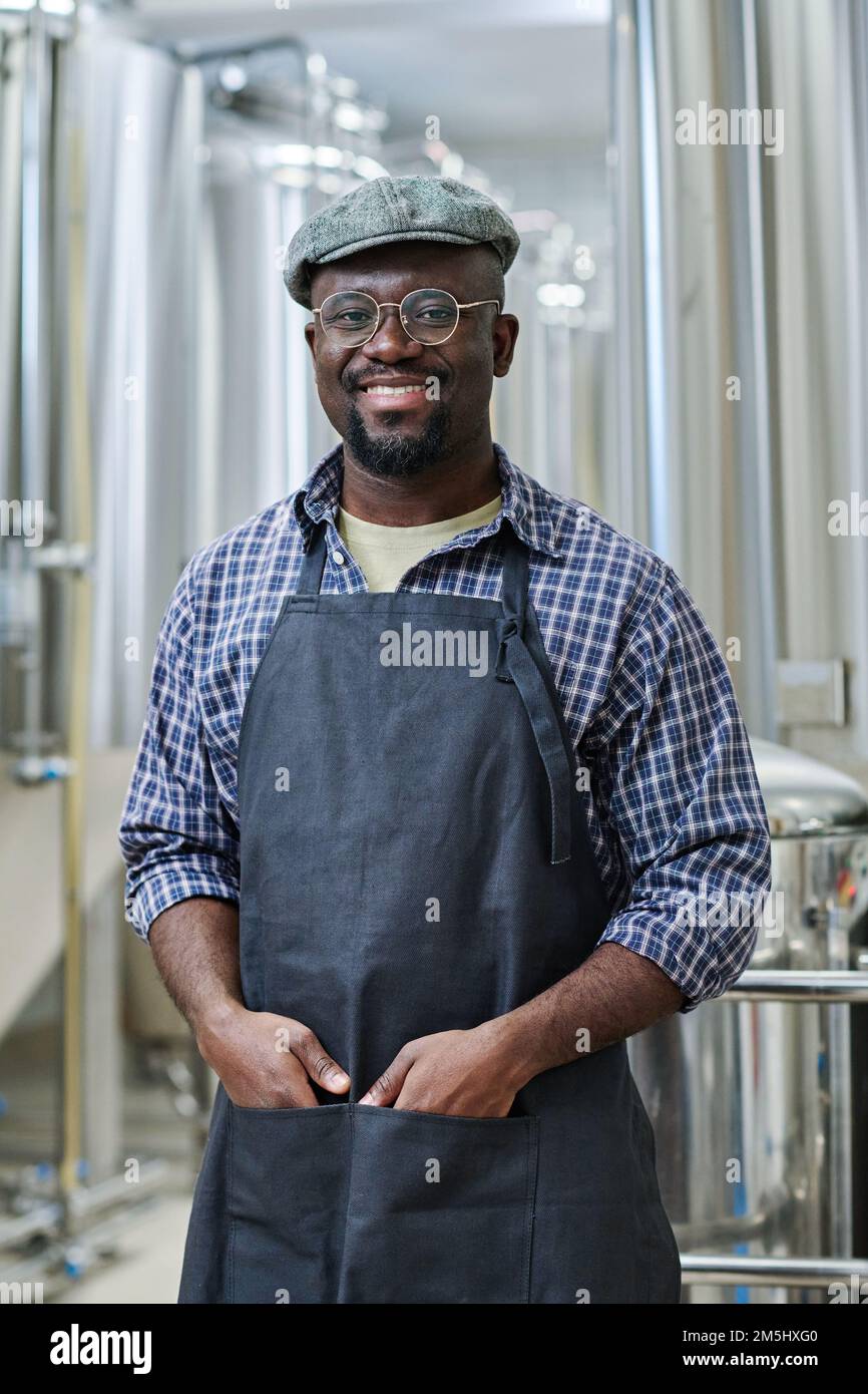 Ritratto dell'uomo afroamericano in uniforme sorridendo alla macchina fotografica, lavora in fabbrica di birra Foto Stock