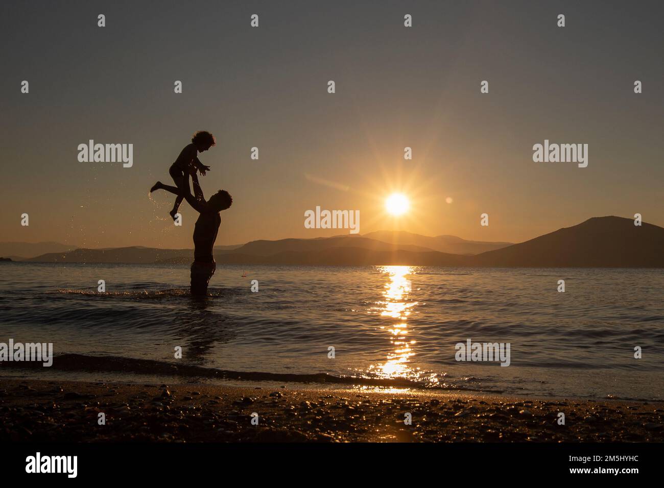 Il padre e il figlio giocano sulla spiaggia che si staglia al tramonto Foto Stock